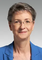Heike Prinz is wearing a blue blazer and glasses, smiling at the camera.